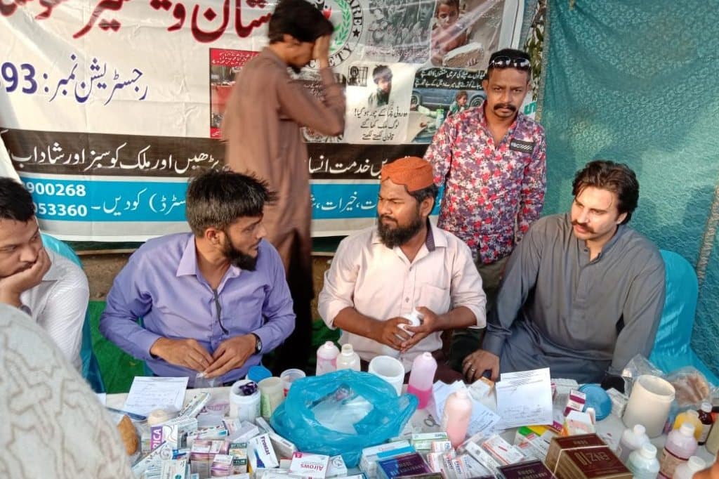 Volunteer doctors at a camp table stacked with donated medicines.