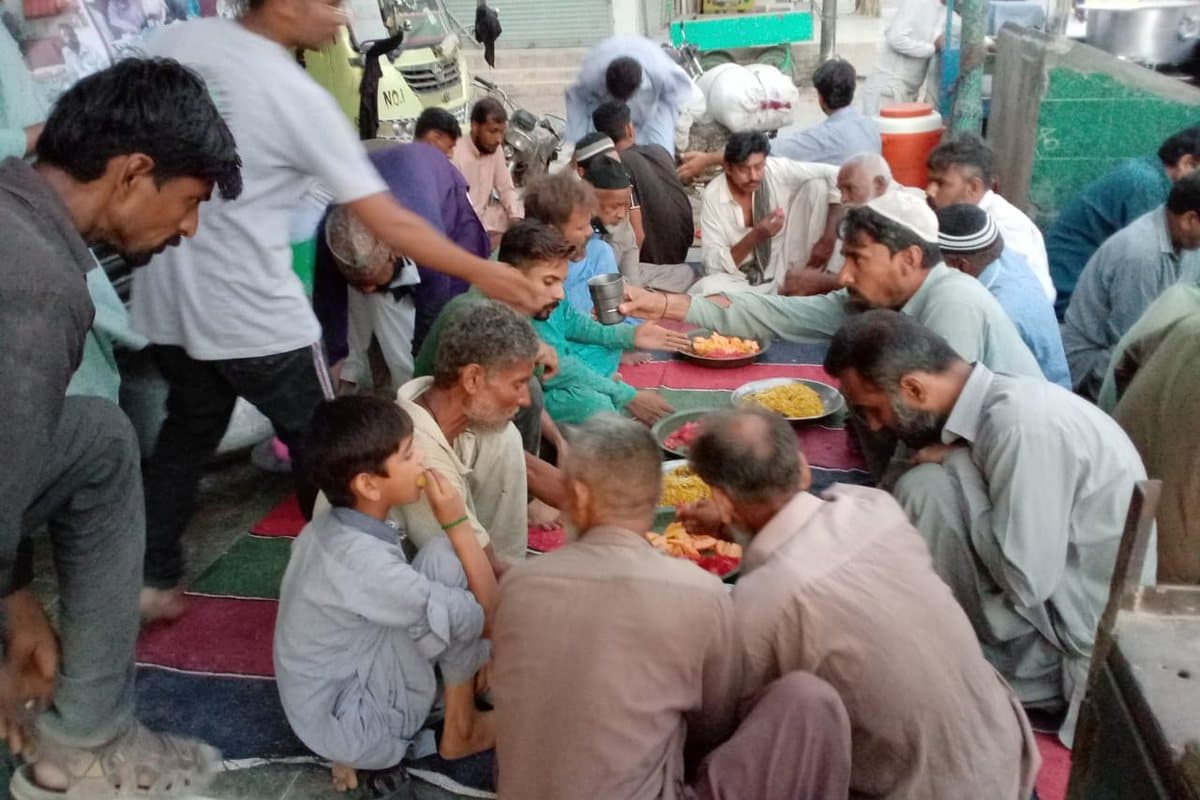 Volunteers serving plates of hot food to people seated at the Dastarkhwan.