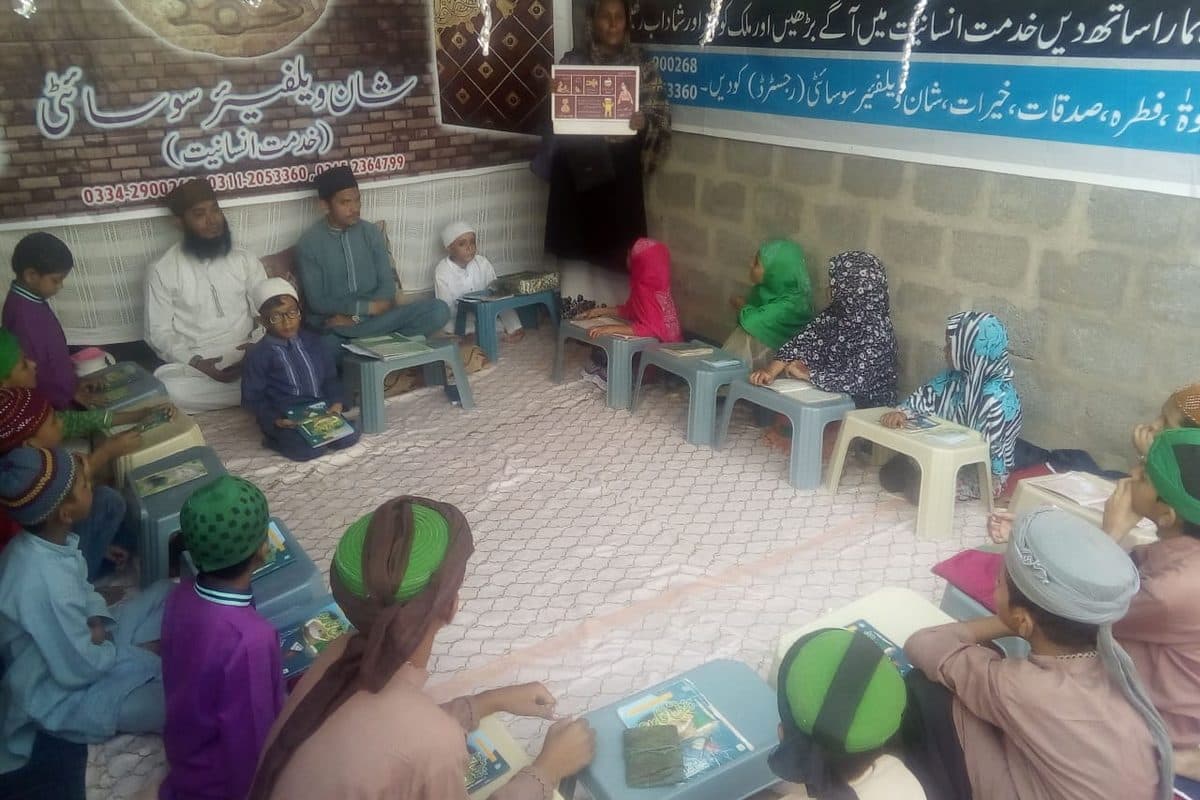 Children seated at low desks reading Qur'ans during a madrasa class.