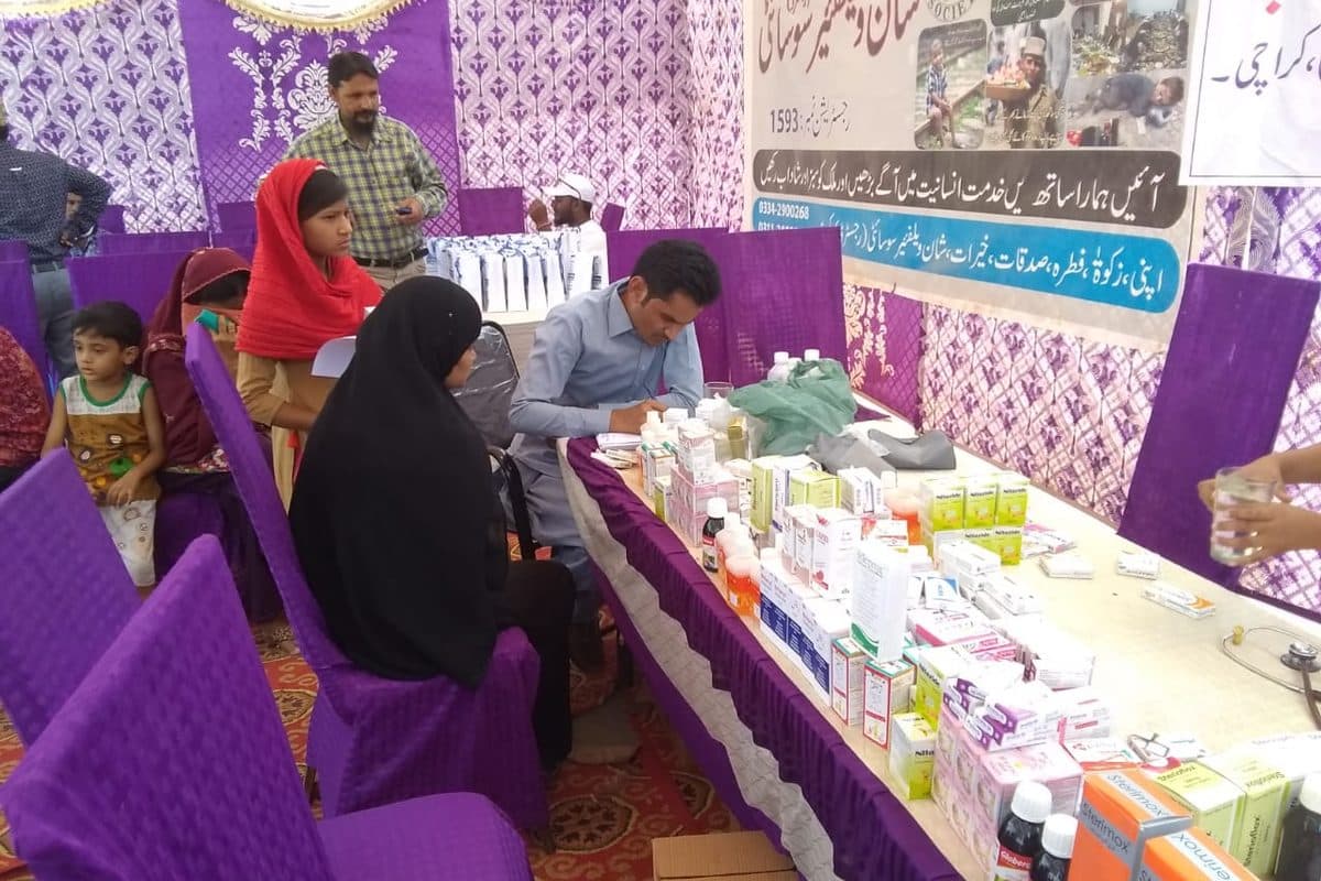 A doctor writing a prescription beside a table of donated medicines at a free medical camp.